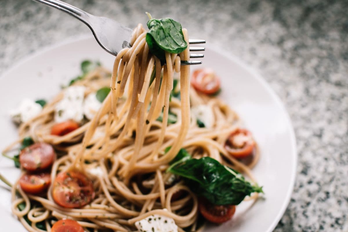 Fork lifting a bite of pasta with cherry tomatoes and basil
