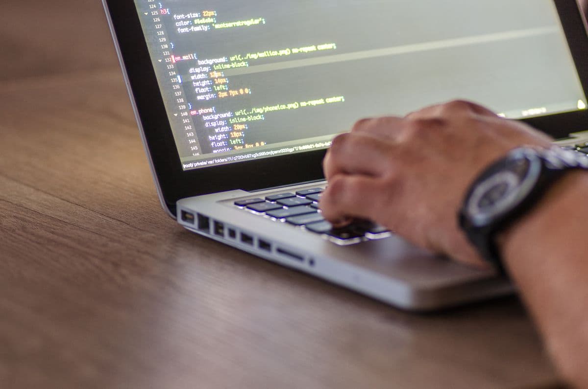 Hands typing on a laptop with code on screen